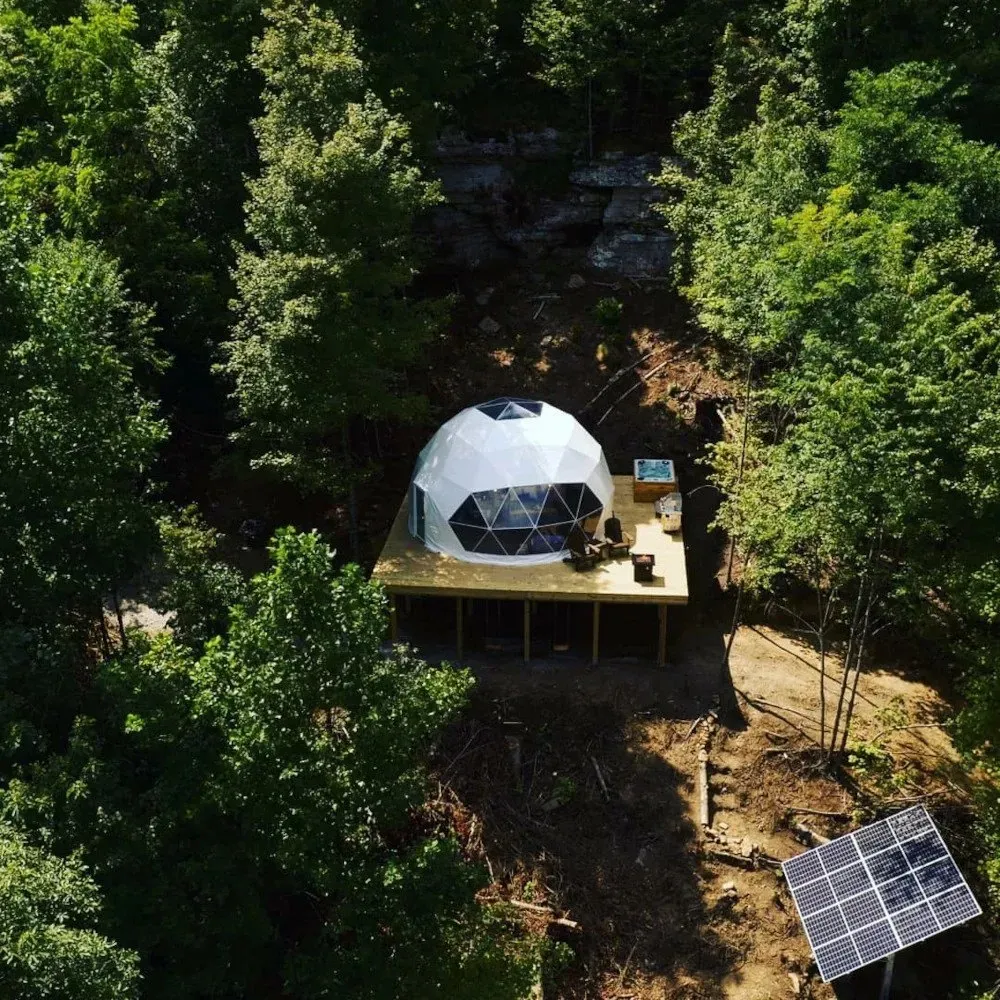 Aerial view of a geodesic dome on a deck in the rainforest, with solar panels beside it